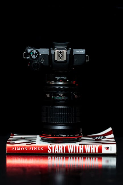 Camera lens placed vertically on Simon Sinek's 'Start with Why' book, against a dark background.